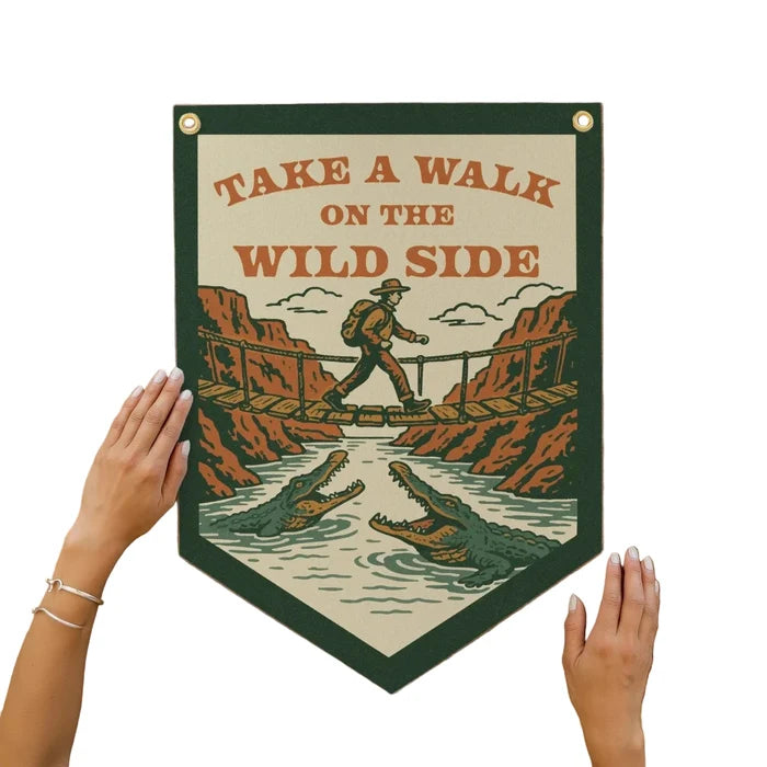 Hand holding Benoit’s Design Co “Take A Walk On The Wild Side” felt pennant with hiker, alligators; adventure decor gift.