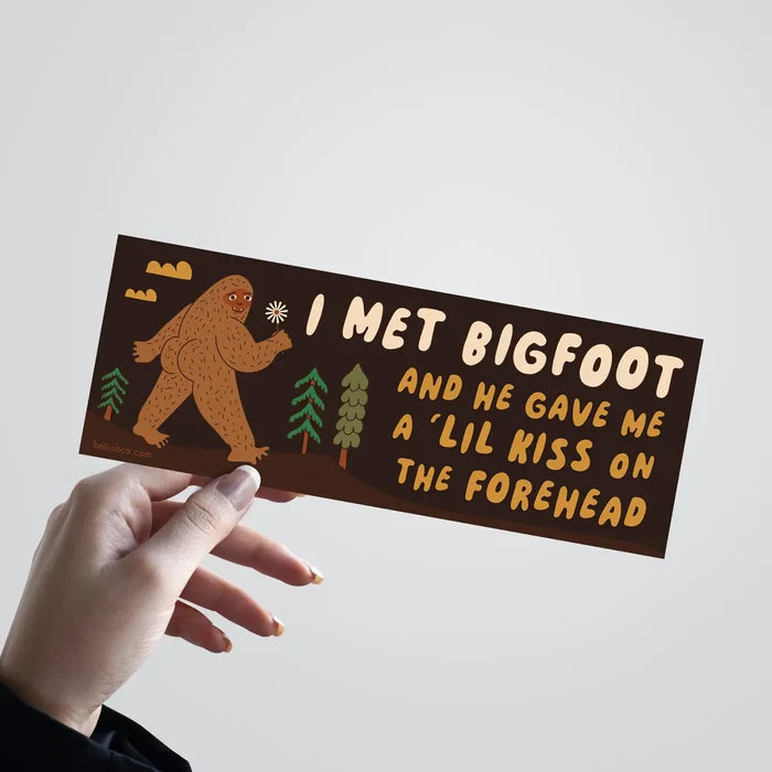 Hand holding Betiobca bumper sticker: “I Met Bigfoot and He Gave Me A Little Kiss” funny sasquatch car decal.
