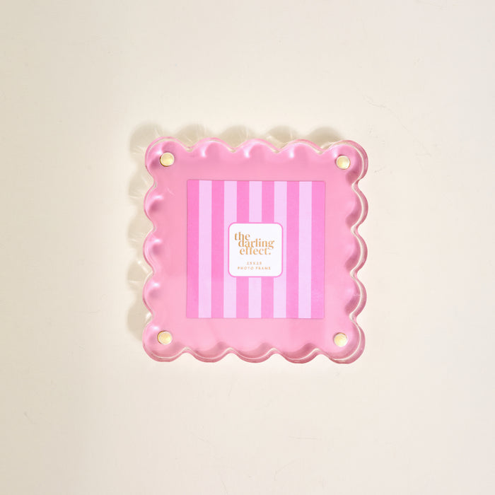 The Darling Effect's Blush Little Moments Acrylic Picture Frame is a pink, square frame with scalloped edges, vertical light and dark pink stripes, and four gold corner accents, shown against a plain light background.