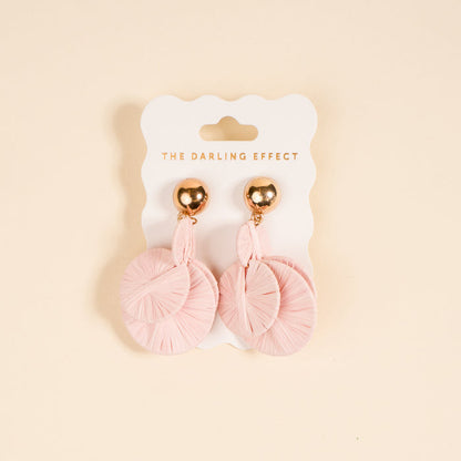 Blush Pretty and Polished Earrings by The Darling Effect feature light pink circular, textured designs on shiny gold studs. Lightweight and ideal for daily wear, they're shown on a branded white card against a beige background.