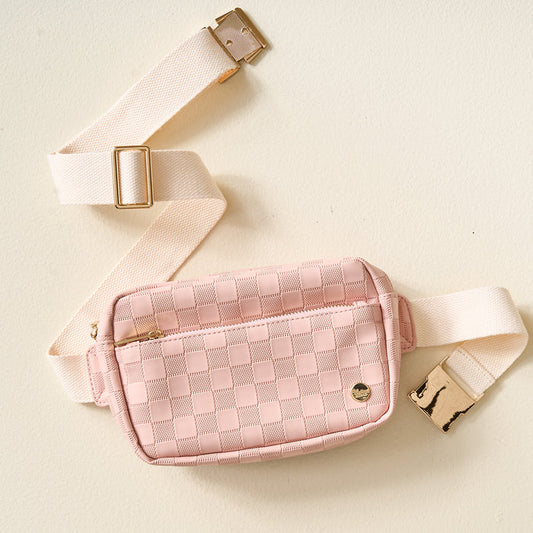 The Darling Effect's Blush Urban Check Belt Bag, featuring a pink checkerboard vegan leather design, cream strap, and gold hardware, is displayed on a light beige background.