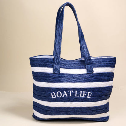 The Darling Effect’s Boat Life Straw & Sun Tote features blue and white stripes with "BOAT LIFE" embroidered on the front—your perfect lightweight vacation tote.