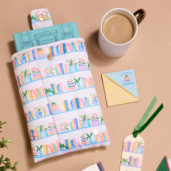 Flat lay of a book in a colorful sleeve with green leaves, a coffee cup, a "Happiness is Reading" card, and two Book Shelfie Acrylic Bookmarks with velvet tassels—a cozy book lover’s scene on a beige surface.