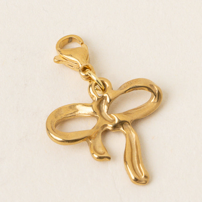 The Bow Jewelry Charm Gold by the-darling-effect features a gold bow design with a lobster clasp, ideal for attaching to bracelets or necklaces. Photographed on a plain light background.