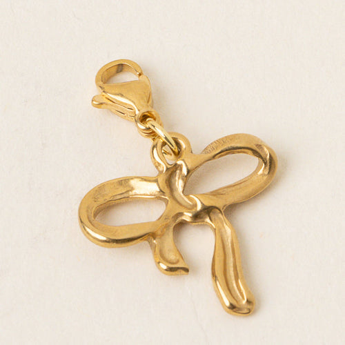 The Bow Jewelry Charm Gold by the-darling-effect features a gold bow design with a lobster clasp, ideal for attaching to bracelets or necklaces. Photographed on a plain light background.
