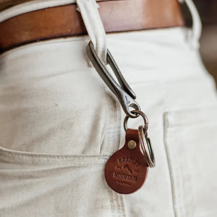 Bradley Mountain Brass Fish Hook Key Fob on a metal clip, hangs from white pants’ belt loop with brown leather belt, stylish keychain.