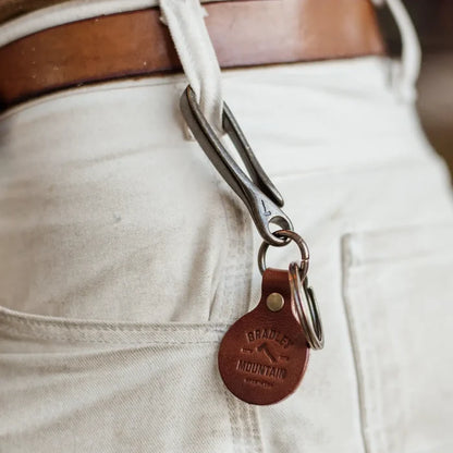 Bradley Mountain Brass Fish Hook Key Fob on a metal clip, hangs from white pants’ belt loop with brown leather belt, stylish keychain.