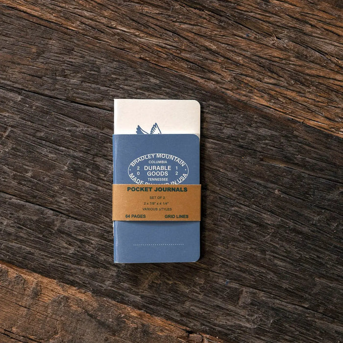 Bradley Mountain Pocket Journals 2 Pack Blue with brown paper band on wood, rugged travel notebooks, durable writing set.