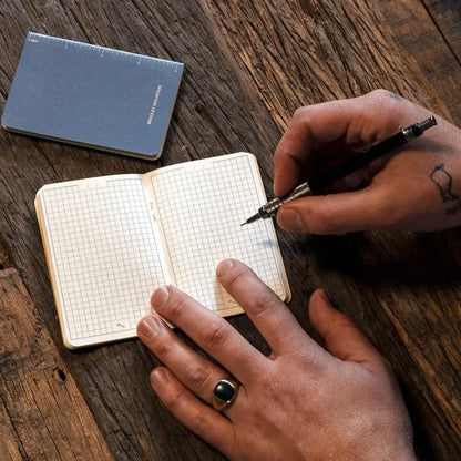 Writing in a Bradley Mountain Pocket Journal—Blue, with its 2-pack set mate on a wooden table; durable travel notebook brand.