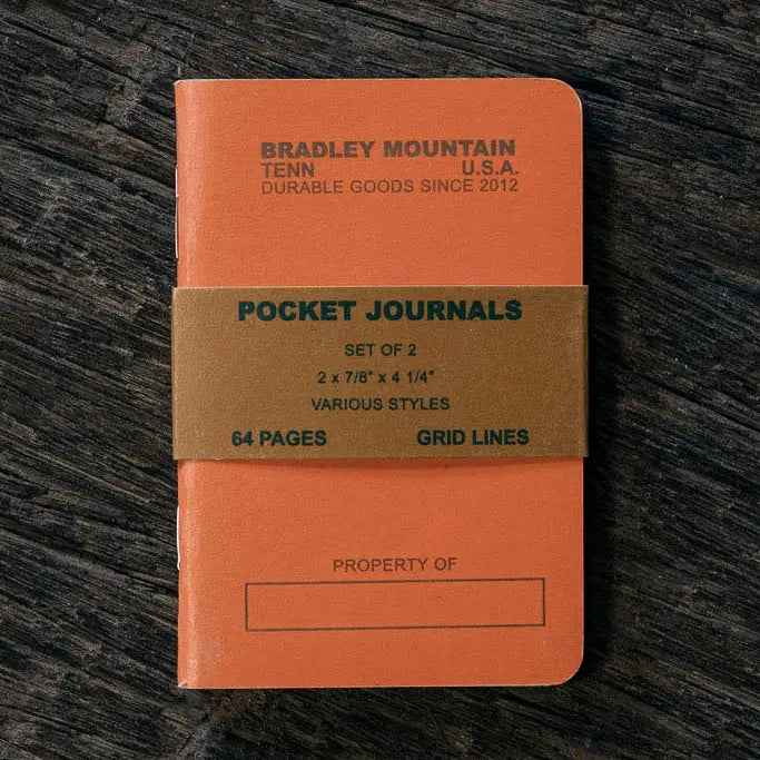 Bradley Mountain Pocket Journals 2 Pack in vibrant orange on a dark wood surface, banded and ready for daily journaling.