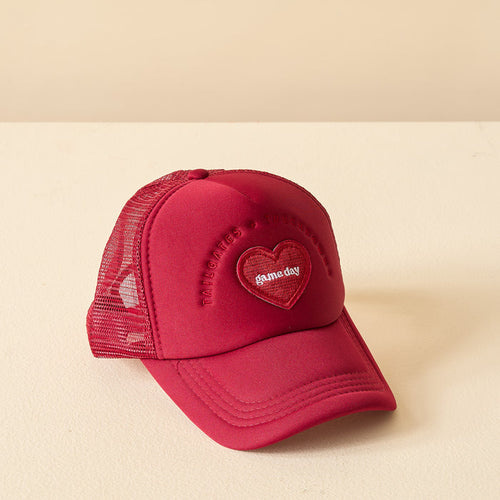 The Darling Effect’s Burgundy Game Day Trucker Hat features a red mesh design, a heart-shaped patch reading “someday,” and “TRANSCRIBES & FOUNDATIONS” embroidered above—ideal for showing team spirit. Displayed on a light surface.