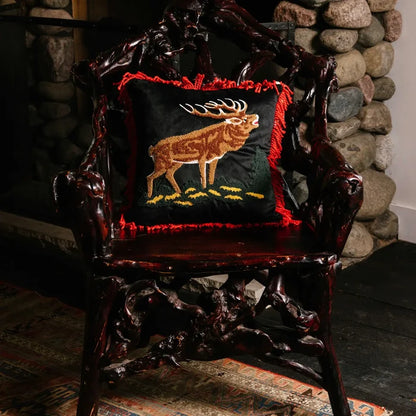 Carved dark wood chair with Peking Camp Wandawega Elk Pillow 18X18, placed beside rustic stone wall. Perfect cozy decor.