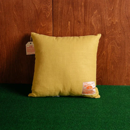 Shop the Peking Camp Wandawega Pointer yellow chainstitched pillow, square with tags, on green carpet by a wood wall.