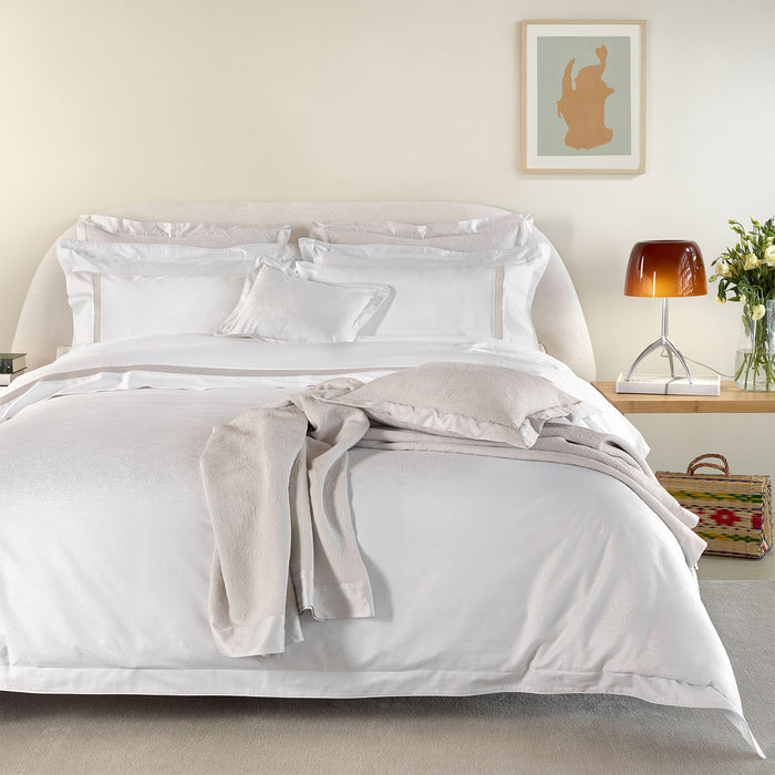 Neatly made bed with Caravela-PaleGrey pillowcase sham and duvet cover in a bedroom setting.