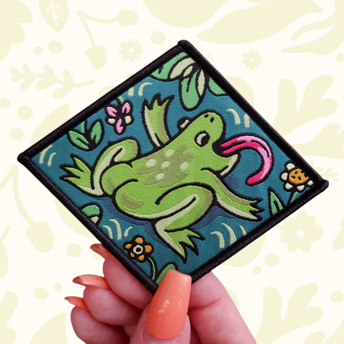 Forager Provisions LTD Cat Coven woven patch featuring a green frog with a long pink tongue on a teal background.