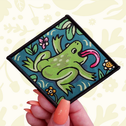 Forager Provisions LTD Cat Coven woven patch featuring a green frog with a long pink tongue on a teal background.