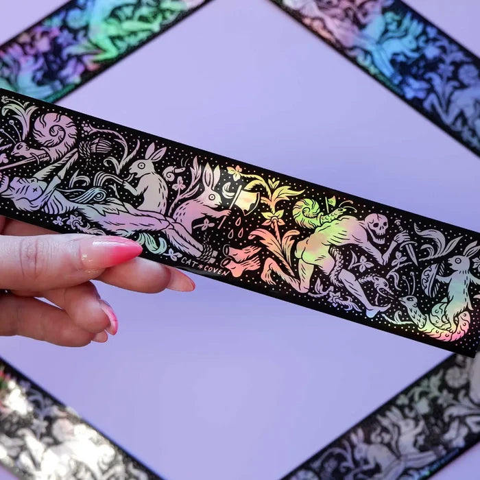 Hand holding Cat Coven holographic sticker featuring fantasy rabbits and skeletons—unique animal art collectible for sticker fans.