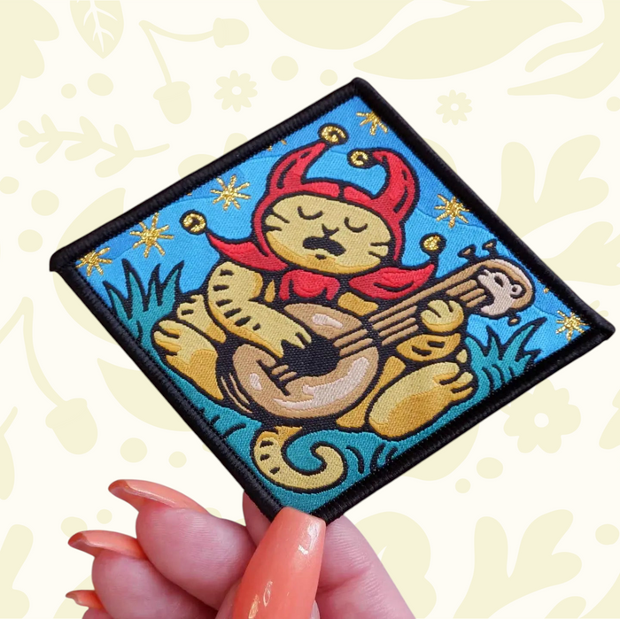 Forager Provisions LTD Cat Coven woven patch featuring a sad jester cat playing a lute on a blue background.