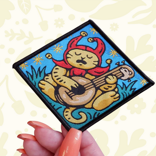 Forager Provisions LTD Cat Coven woven patch featuring a sad jester cat playing a lute on a blue background.