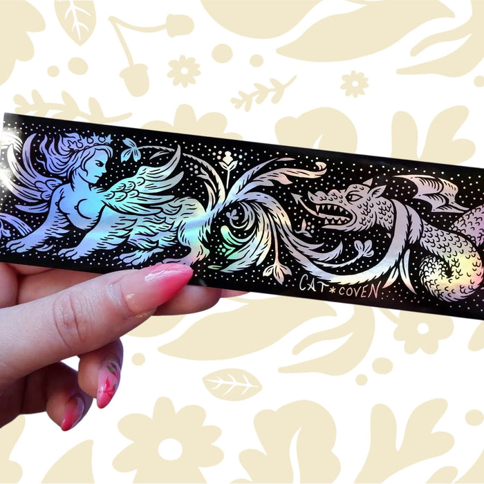 A hand displays a holographic Cat Coven Sphinx vs Dragon sticker with mythical creature art, unique fantasy collectible.