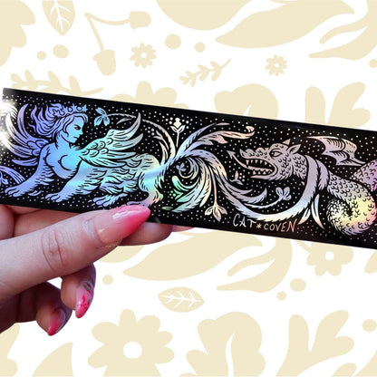 A hand displays a holographic Cat Coven Sphinx vs Dragon sticker with mythical creature art, unique fantasy collectible.