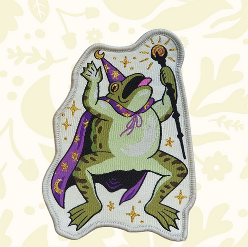 Forager Provisions LTD Cat Coven woven patch featuring a green toad wizard in a purple cape with gold star details.