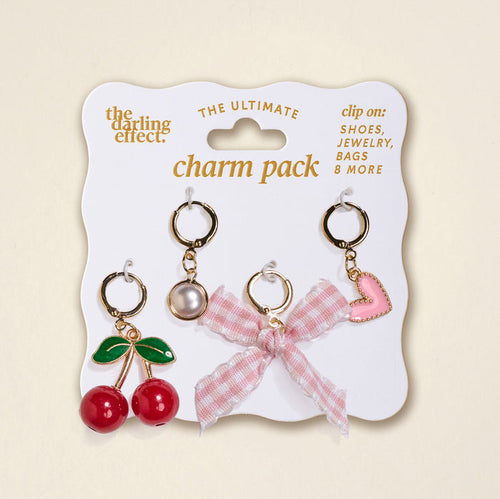 The Darling Effect’s Cherry on Top The Ultimate Charm Pack includes four clip-on charms—red cherries with green leaves, a pearl, a pink gingham bow, and a pink heart with gold trim—to personalize your scrunchie charm sets. Displayed on a branded white card.