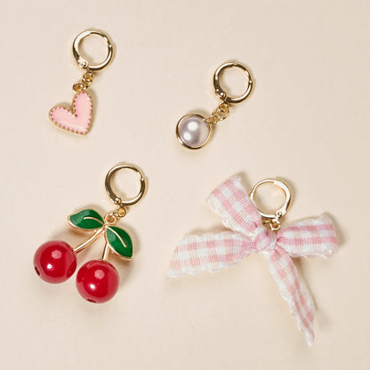 The Darling Effect’s Cherry on Top The Ultimate Charm Pack features four gold hoop charms—a pink heart, white pearl, red cherries with green leaves, and a pink-and-white gingham bow—perfect for scrunchie charm sets or accenting statement necklaces. Shown on beige.