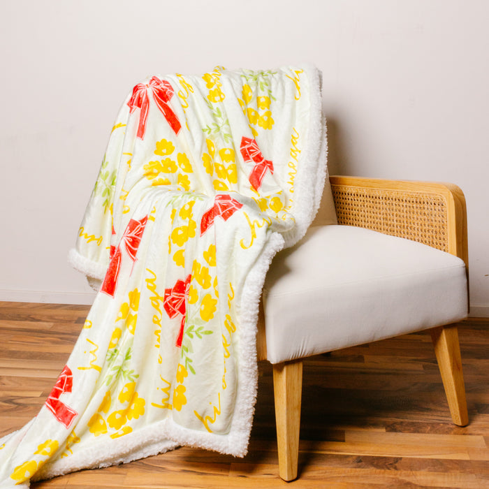 The Chi Omega Plush Sherpa Blanket by The Darling Effect, featuring yellow and red floral patterns, is draped over a modern cane-back chair—ideal as a cozy sorority or college dorm blanket.