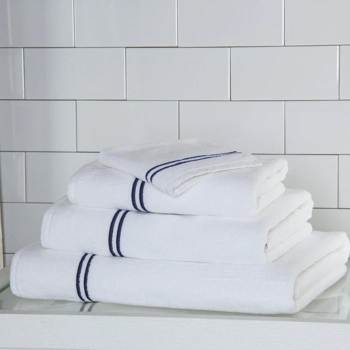 a white navy Classic Bath towel stacked on classic towels on a white surface and platform pattern wall