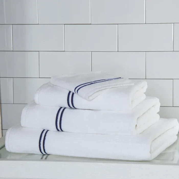 a white navy Classic guest towel stacked on classic towels on a white surface and platform pattern wall
