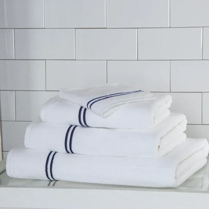 a white navy Classic guest towel stacked on classic towels on a white surface and platform pattern wall