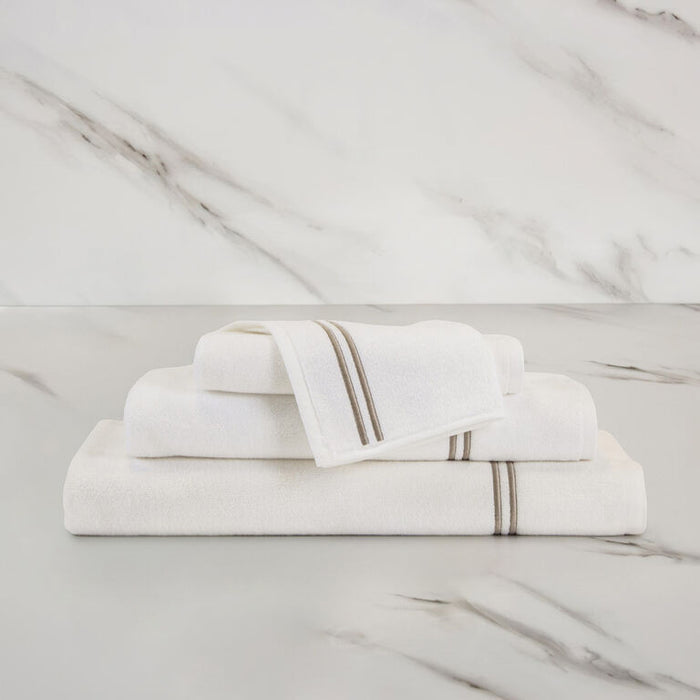 unfolded white khaki classic wash cloth stacked on other classic towels on a marbeled surface and background