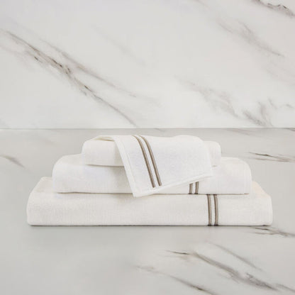unfolded white khaki classic wash cloth stacked on other classic towels on a marbeled surface and background
