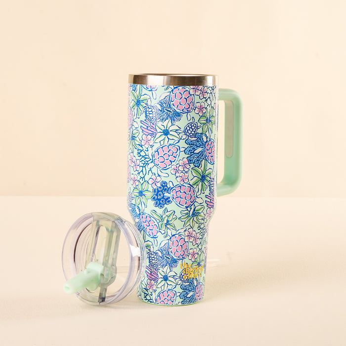 The-darling-effect Coastal Cove 40 oz Lifestyle Flip Straw Tumbler with a vibrant floral and fruit pattern, mint green handle, and matching flip lid with clear top, sits on a light surface against a beige background.