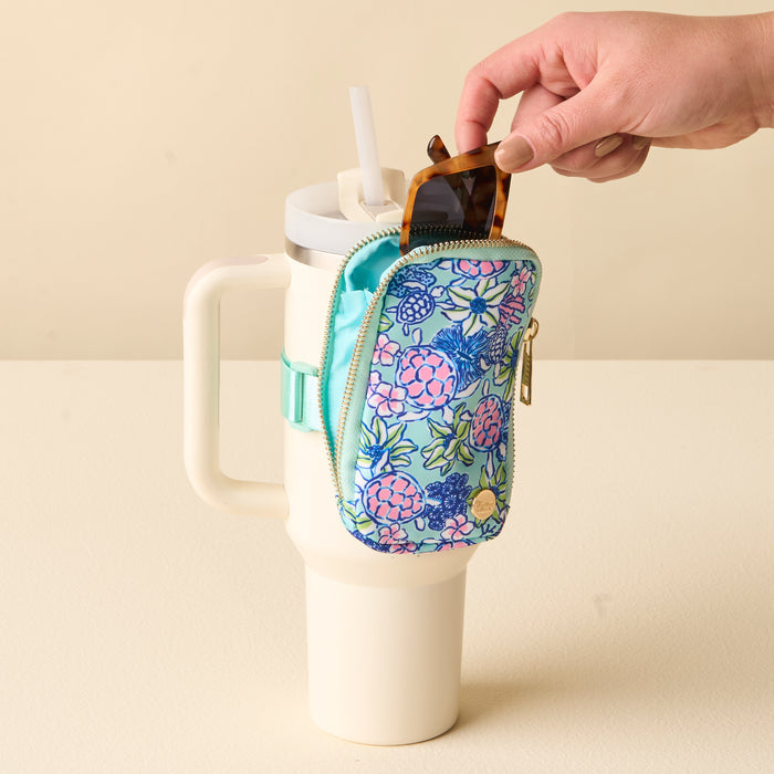 A hand places sunglasses into a Coastal Cove Tumbler Fanny Pack by the-darling-effect, which is attached to the side of a large white travel mug with a handle and straw.