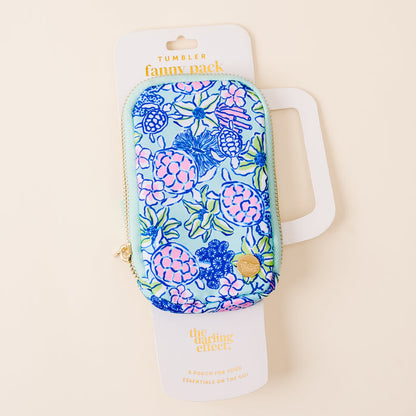 A colorful, floral Coastal Cove Tumbler Fanny Pack from the-darling-effect sits on a cream background with branded packaging and a gold heart-shaped zipper pull—this bestselling, water-resistant accessory is perfect for any outing.