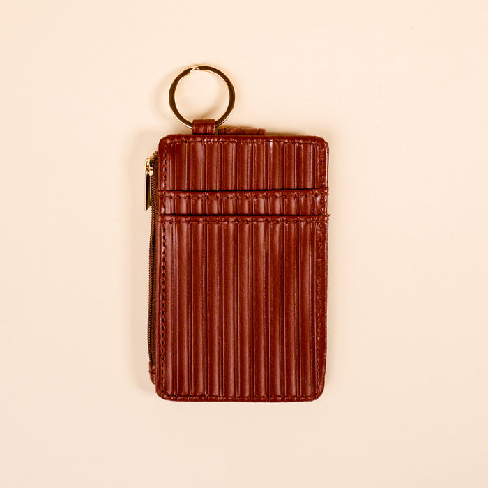 The Darling Effect's Cognac Ripple Ridge Keychain Wallet features brown, vertically-ribbed leather, a zipper pocket, and a gold key ring, shown on a plain beige background.