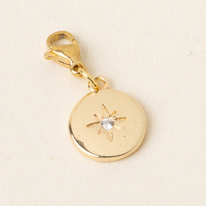 The-darling-effect's Compass Jewelry Charm Gold features a round design with an engraved starburst and a clear gemstone at the center, finished with a lobster clasp—perfect for your charm bar. Displayed on a light background.