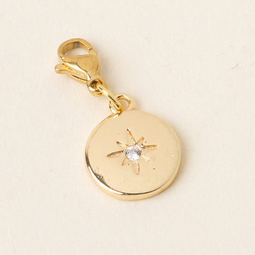 The-darling-effect's Compass Jewelry Charm Gold features a round design with an engraved starburst and a clear gemstone at the center, finished with a lobster clasp—perfect for your charm bar. Displayed on a light background.