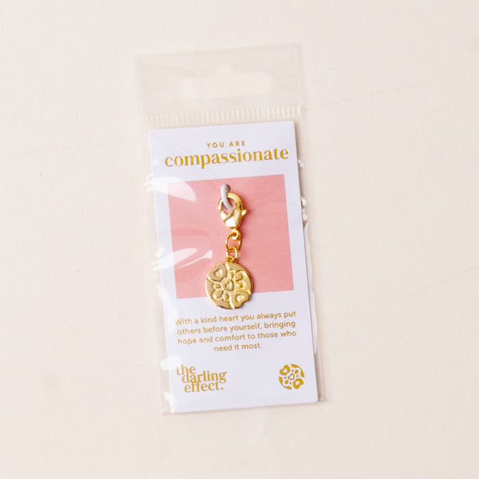 The-darling-effect Compassionate Jewelry Trait Charm Gold comes with a clasp, packaged on a card stating "You are compassionate" with the brand’s logo below, all inside a clear plastic sleeve.