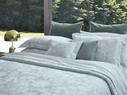 Copacabana pillowcase and duvet cover jade on a bed in a room with large windows showing greenery outside.