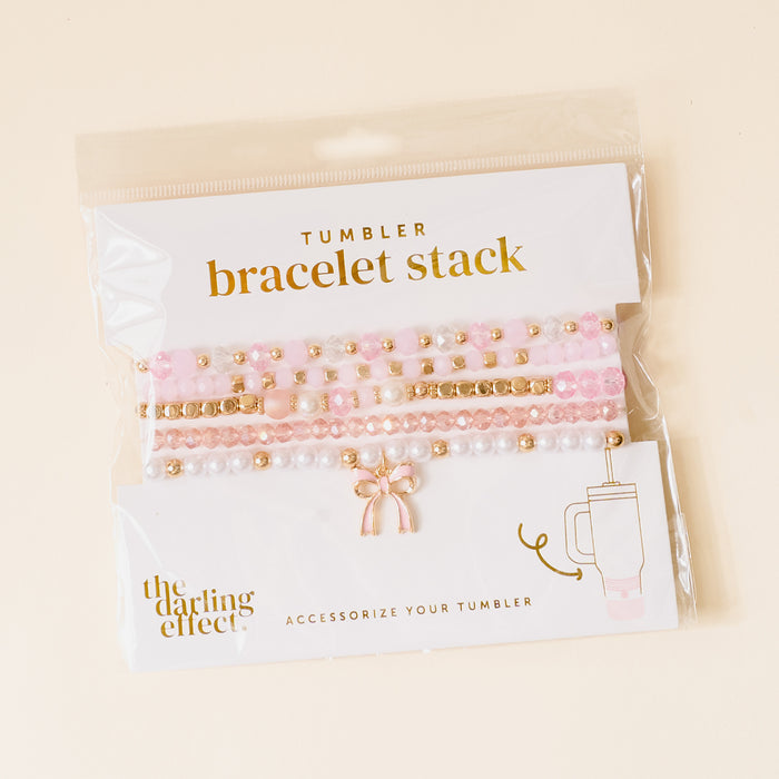 The Coquette Charm Tumbler Bracelet Stack by the-darling-effect features pink, white, and gold beaded bracelets—stylish accessories for your 40 oz tumbler, shown against a light beige background.