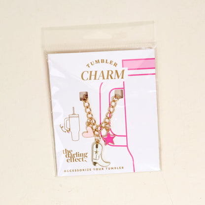 The Cowgirl Tumbler Charm by the-darling-effect features a white cowboy boot, pink heart, and pink star on a gold chain, displayed on a white card with pink accents—perfect for adding fun style to your drinkware.
