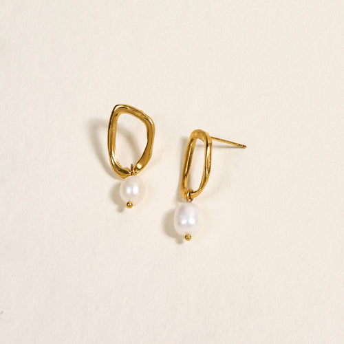 The Darling Effect's Dainty Drift Standout Earrings, featuring irregular shapes and white pearls, shine against a cream background—perfect for special occasions.