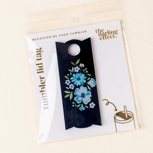 The Dainty Floral Navy Tumbler Lid Tag by the-darling-effect features a blue and white floral design on black, packaged on a white card labeled "tumbler lid tags"—ideal for those who love personalized drinkware.