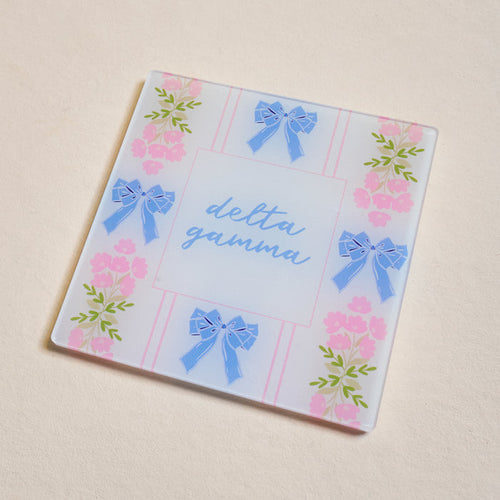The Darling Effect’s Delta Gamma Acrylic Coaster features blue script, blue bows, and pink flowers on a pastel background—an ideal and charming Big/Little gift for any sorority member.