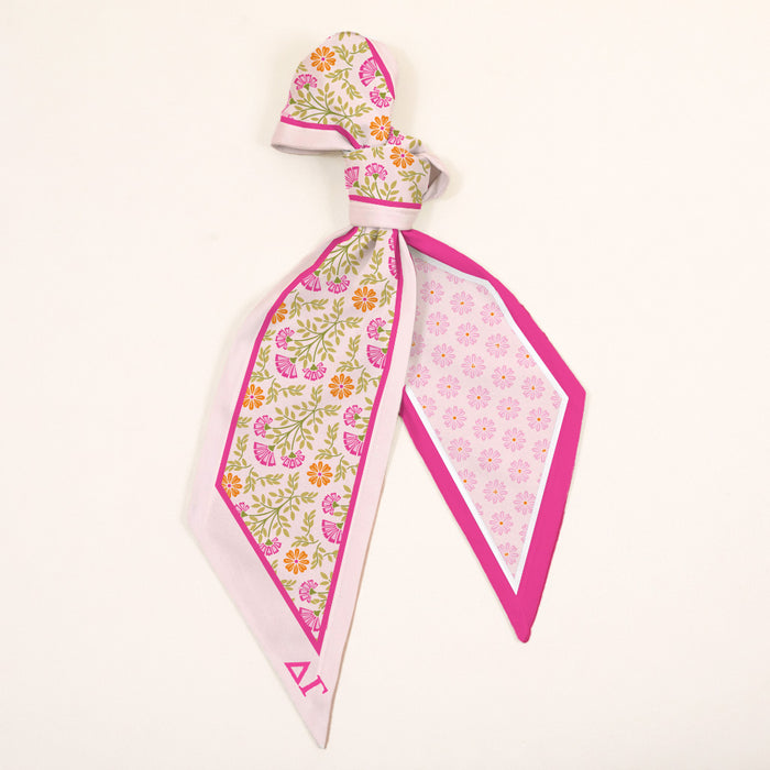 The Darling Effect’s Delta Gamma Twirl & Tie Scarf Accessory features pink, yellow, and green florals with a bright pink border and a geometric pattern—an elegant, versatile accent perfect for any look.