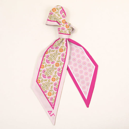The Darling Effect’s Delta Gamma Twirl & Tie Scarf Accessory features pink, yellow, and green florals with a bright pink border and a geometric pattern—an elegant, versatile accent perfect for any look.