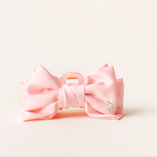 The Darling Effect’s Delta Zeta Satin Bow Claw Clip in pale pink, featuring “AZ” in light green, sits upright against a white background—an ideal accessory to add charm to your updos.